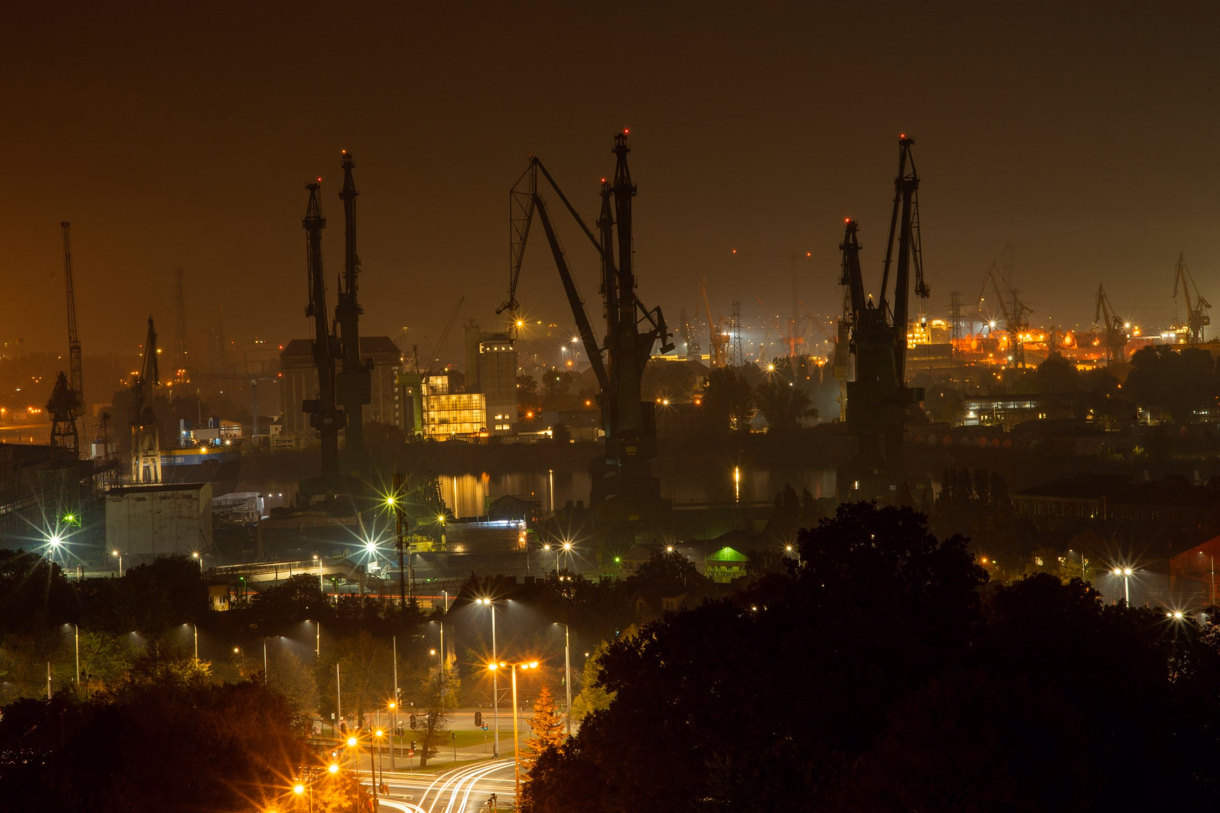 Construction cranes at night against a lit downtown skyline.