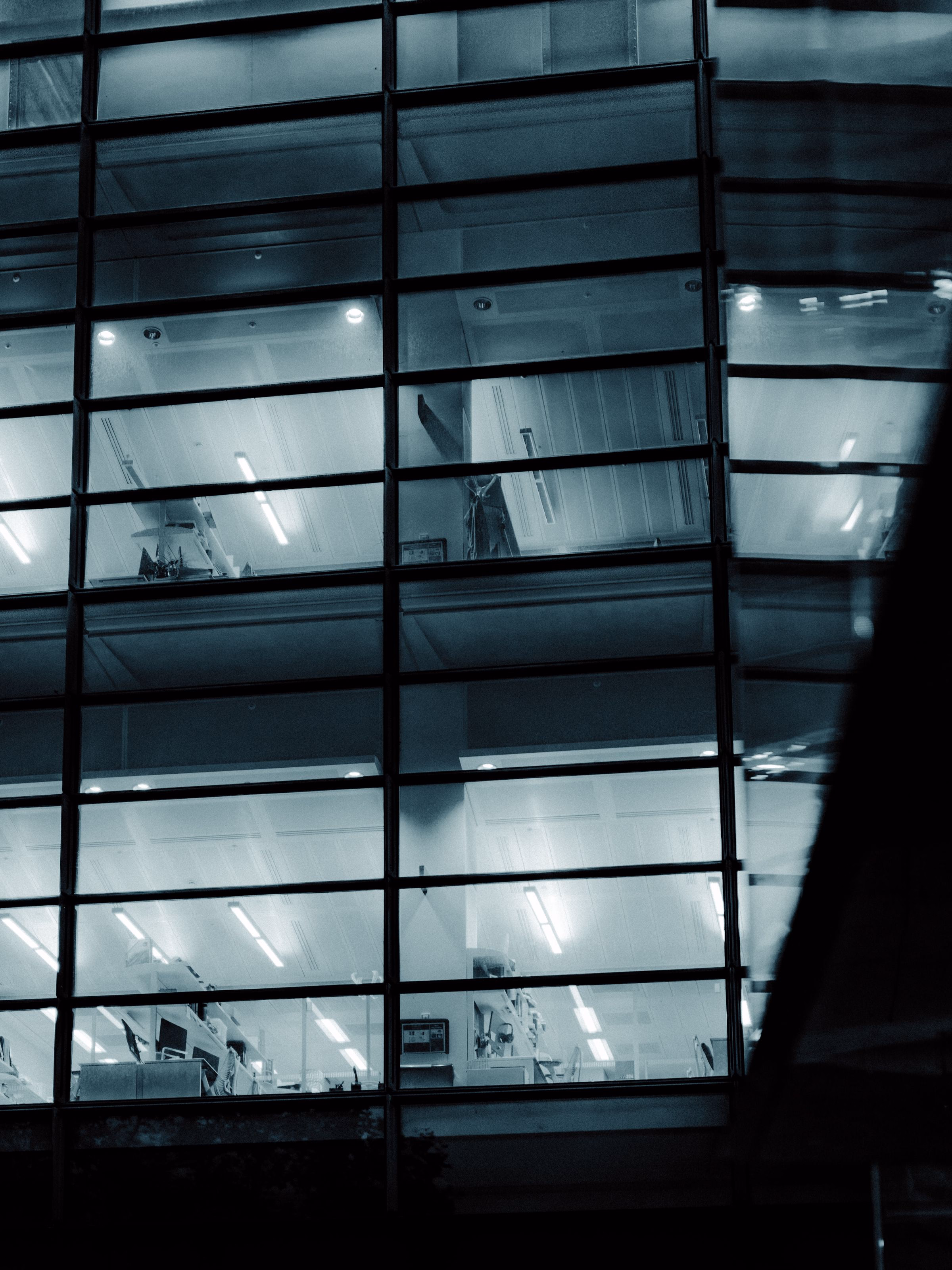 Glass office façade lit from within at night, geometric reflection.