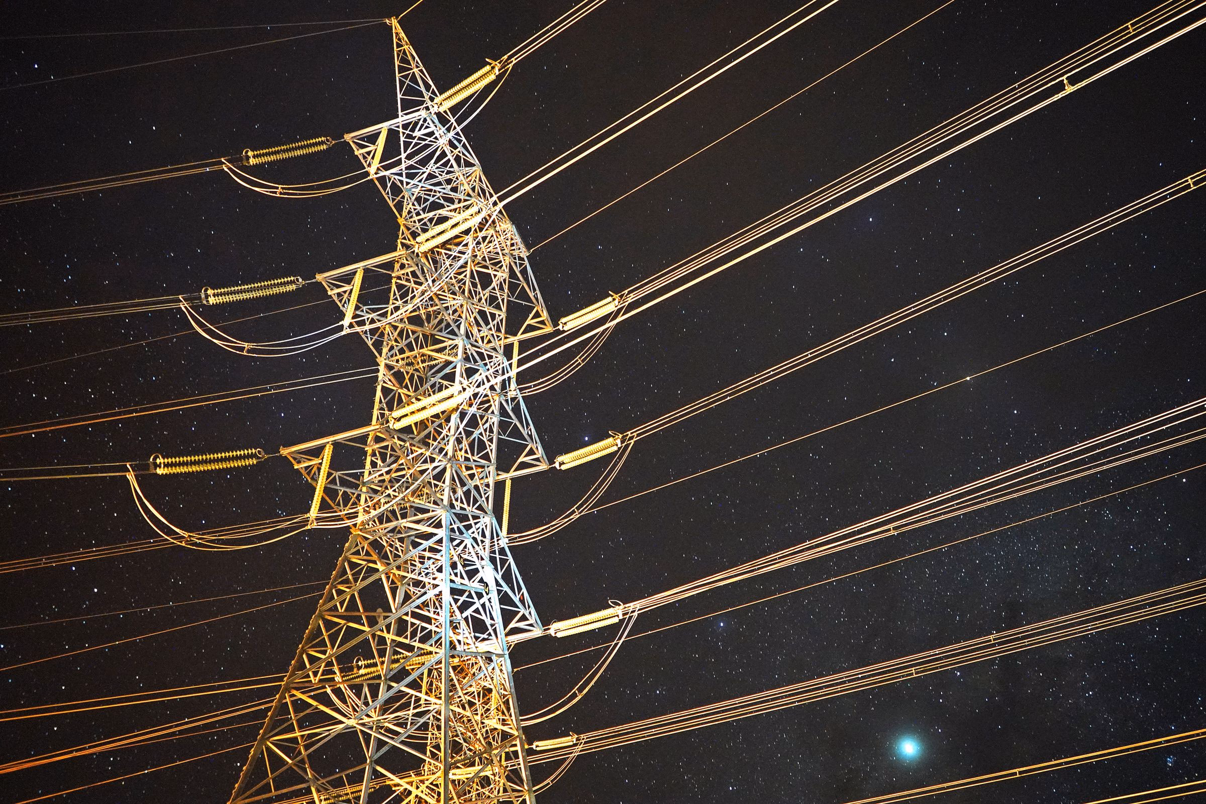 High-voltage transmission tower lit warmly against a starry night sky.